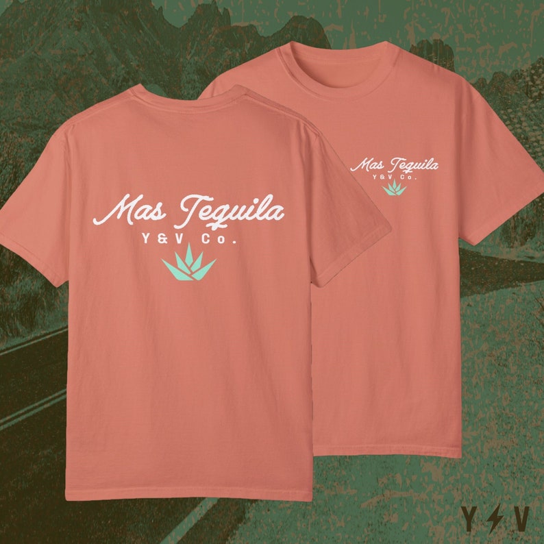 May include: A coral coloured t-shirt with a white graphic that says "Mas Tequila Y&V Co." with a green agave plant design. The shirt is shown on a model with the back of the shirt facing the viewer.