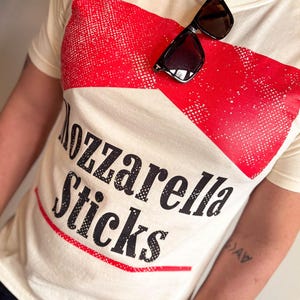 May include: A white t-shirt with a red and white graphic that says "Mozzarella Sticks".