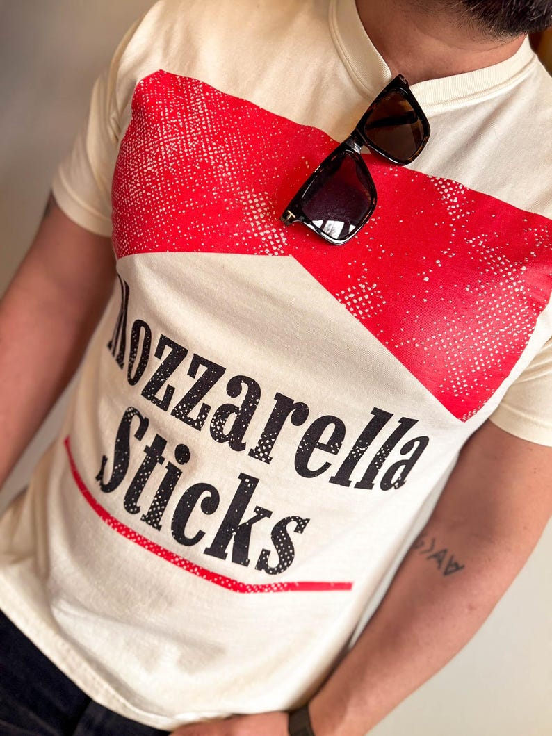 May include: A white t-shirt with a red and white graphic that says "Mozzarella Sticks".