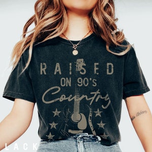 May include: Black t-shirt featuring a distressed graphic design that reads "Raised on 90's Country" with a vintage guitar illustration.