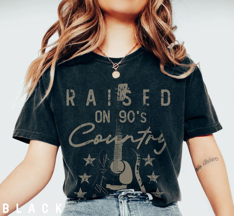 May include: Black t-shirt featuring a distressed graphic design that reads "Raised on 90's Country" with a vintage guitar illustration.
