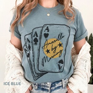 May include: A blue t-shirt with a graphic of four playing cards with the text "Amarillo by Morning" in a circle with stars.