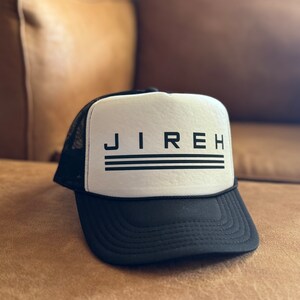 May include: A black and white trucker hat with the word "JIREH" in black letters on the front. The hat has a black mesh back and a white front panel.