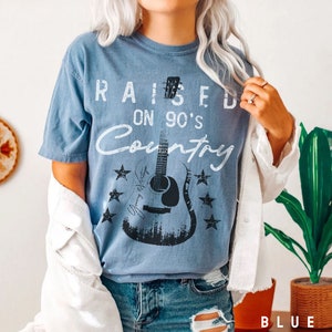 May include: A blue t-shirt with a distressed white graphic that says "Raised on 90's Country" with a black silhouette of a guitar and stars.