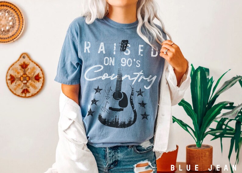 May include: A blue t-shirt with a distressed white graphic that says "Raised on 90's Country" with a black silhouette of a guitar and stars.