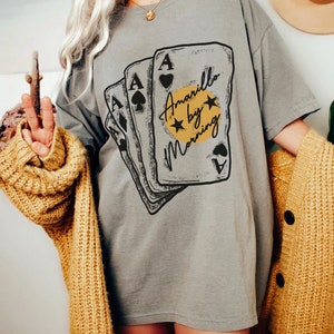 May include: A grey t-shirt with a graphic of four playing cards with the text "Amarillo by Morning" on the front.