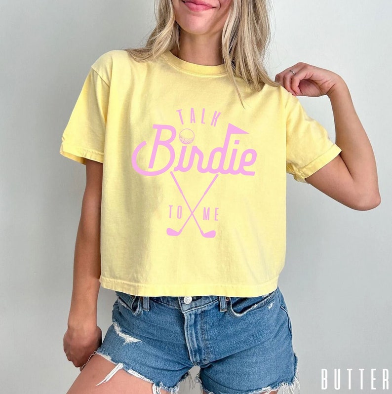 May include: Yellow cropped t-shirt with a pink graphic that says "Talk Birdie To Me" with a golf ball and golf clubs.
