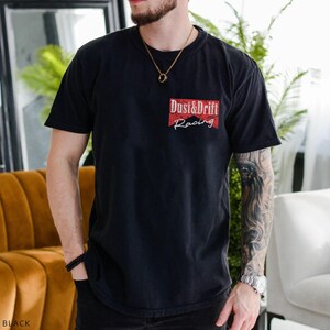 May include: Black short-sleeve t-shirt with a red and white graphic that reads "Dust & Drift Racing". The shirt is a crew neck style and appears to be made of a soft material. The word "BLACK" is at the bottom left of the image.