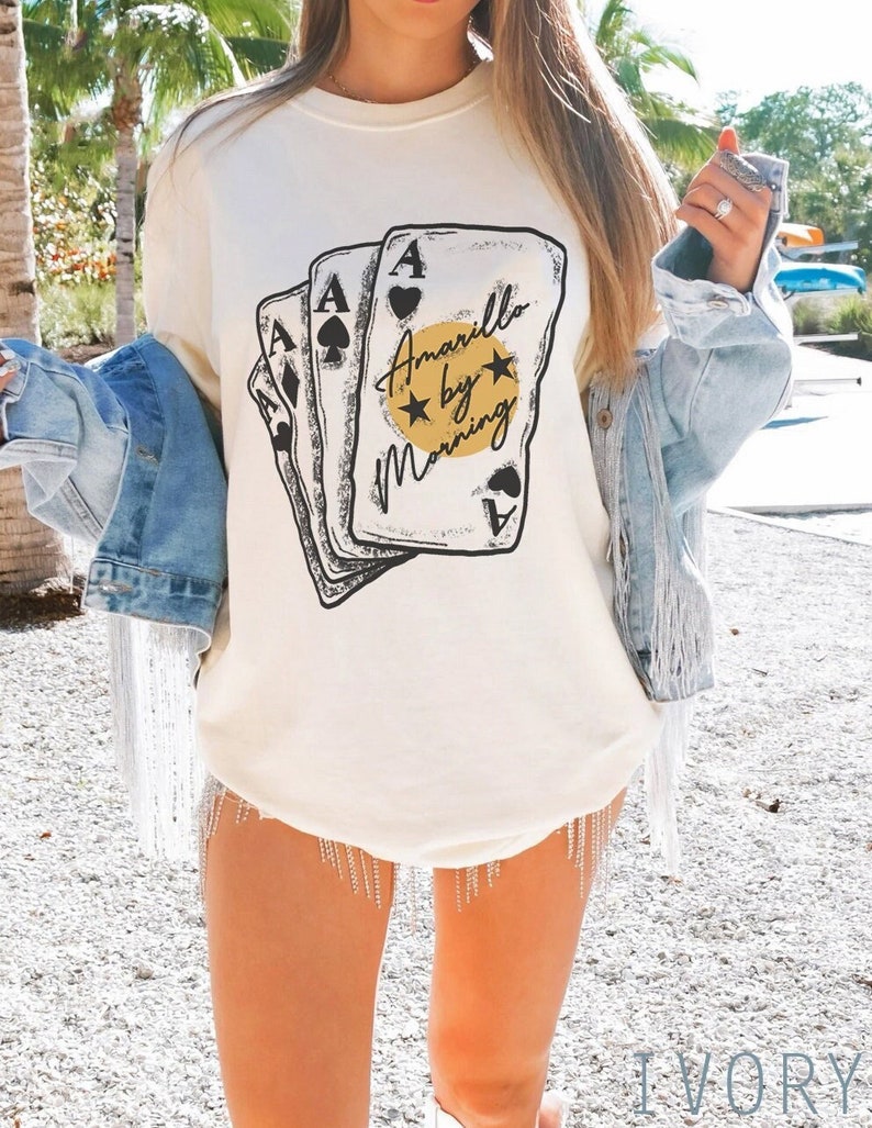 May include: Ivory white long-sleeve t-shirt with a graphic of four playing cards and the text "Amarillo by Morning".