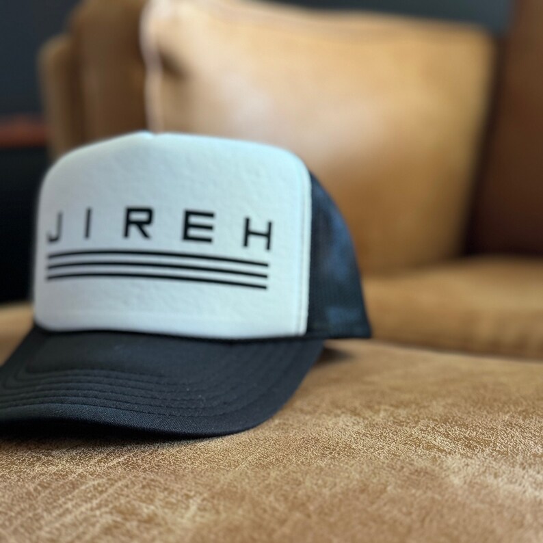 May include: A black and white trucker hat with the word "JIREH" in black lettering on the front. The hat has a black mesh back.