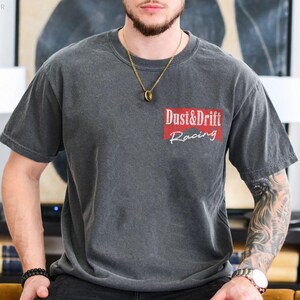 May include: Dark gray t-shirt with the text "Dust & Drift Racing" in white and red. The shirt has a crew neck and short sleeves. The shirt is made of a soft, comfortable material.