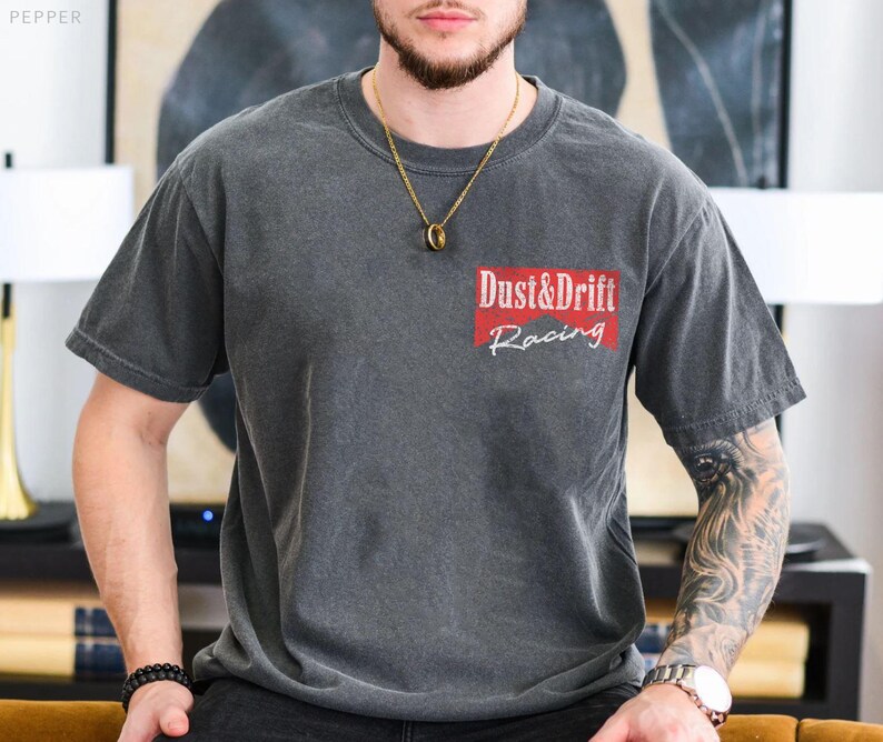 May include: Dark gray t-shirt with the text "Dust & Drift Racing" in white and red. The shirt has a crew neck and short sleeves. The shirt is made of a soft, comfortable material.