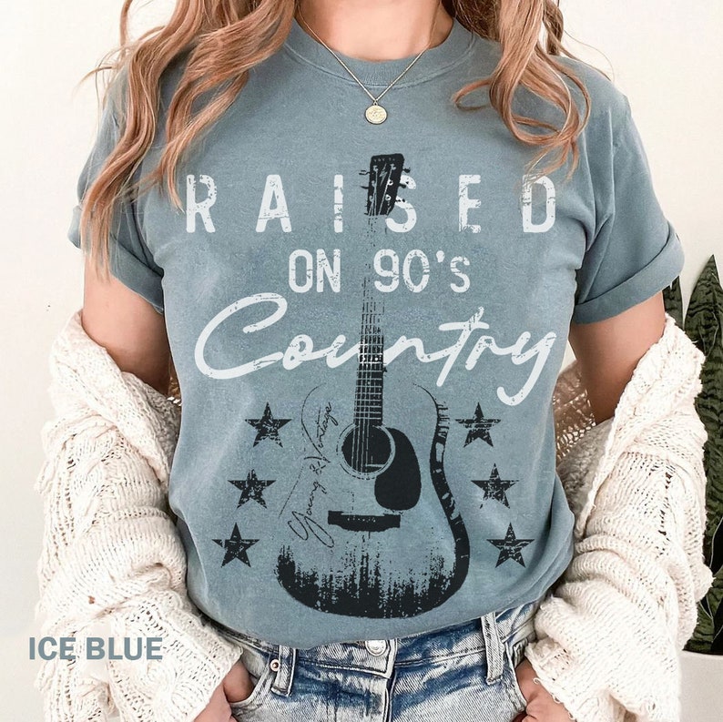 May include: A light blue t-shirt with the text "RAISED ON 90'S COUNTRY" in white. A black and white silhouette of a guitar is in the centre of the shirt with stars around it.