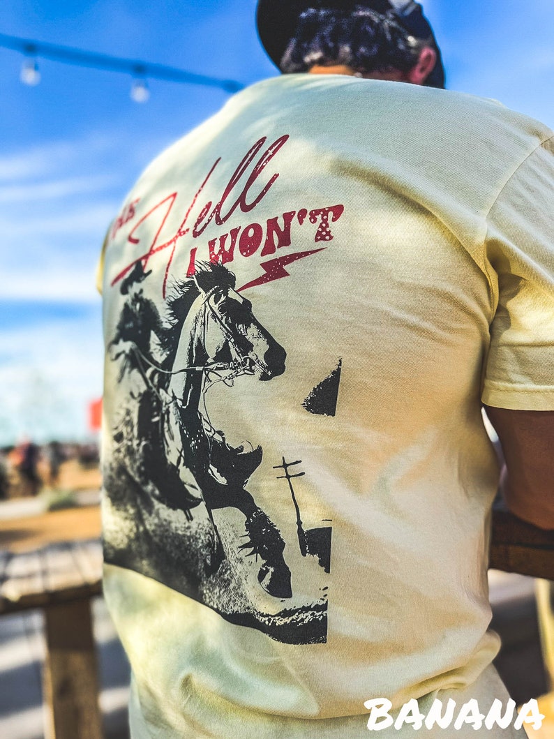 Peut inclure: Un t-shirt jaune clair avec une image en noir et blanc d'un cow-boy &agrave; cheval. Le texte "This Hell I Won't" est imprim&eacute; en rouge sur le t-shirt.