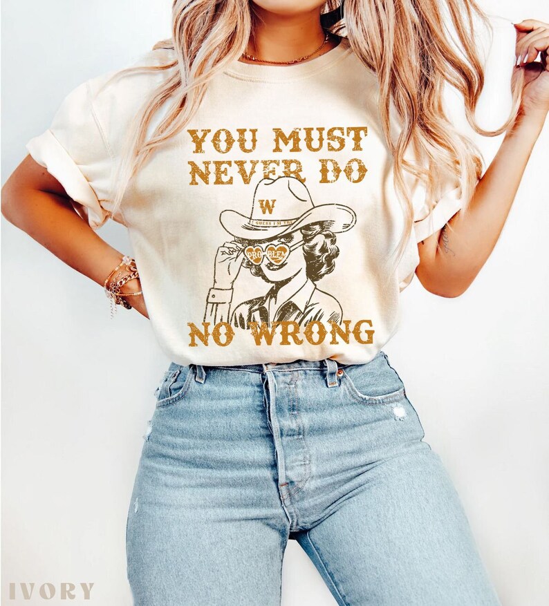 May include: A white t-shirt with the text "You must never do no wrong" and a drawing of a woman wearing a cowboy hat and sunglasses with the text "W" on the hat. The text is in brown and the drawing is in black and brown.