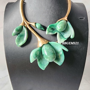 May include: A striking necklace with a floral motif. The necklace features a gold-coloured chain and branches, adorned with green marbled resin flowers and leaf details. The text "BBGEMS21" is visible on the right side of the image.