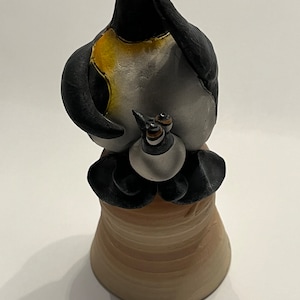 May include: A ceramic penguin figurine with a yellow chest and black eyes. The penguin is sitting on a brown ceramic base.