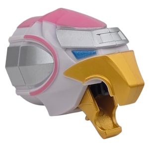 Peut inclure: Gros plan sur une tête de robot jouet, avec un schéma de couleurs blanc, rose, argent et or. La tête présente un design stylisé avec des formes géométriques et une structure en forme de bec. L'esthétique générale suggère un thème futuriste ou mécanique.