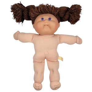 Pode incluir: Uma boneca Cabbage Patch Kid com cabelo castanho em rabo de cavalo, vestindo uma roupa de cor nude. A boneca tem olhos azuis e um sorriso pintado.