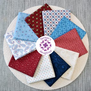 May include: A collection of folded fabric squares in various patriotic patterns, including stars, paisley, and floral designs. The fabrics are arranged in a circular pattern on a white woven mat. The center features a logo with the text "farmer's daughter".