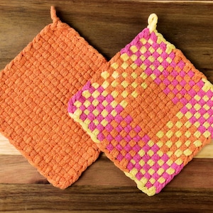 May include: Two orange and yellow knitted pot holders. One pot holder has a checkered pattern with pink and yellow squares. The other pot holder is a solid orange color.