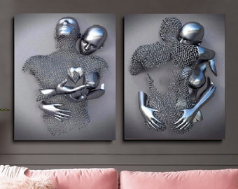 Op de afbeelding: Twee zilveren sculpturen van figuren die elkaar omhelzen. De sculpturen zijn gemaakt van een gaasachtig materiaal en worden getoond op een grijze achtergrond.