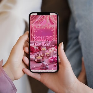 May include: A smartphone displays a pink invitation scene with the text "YOU'RE invited..." in a neon style. The scene includes a bed with pillows, candles, and popcorn. The phone is held by a person.