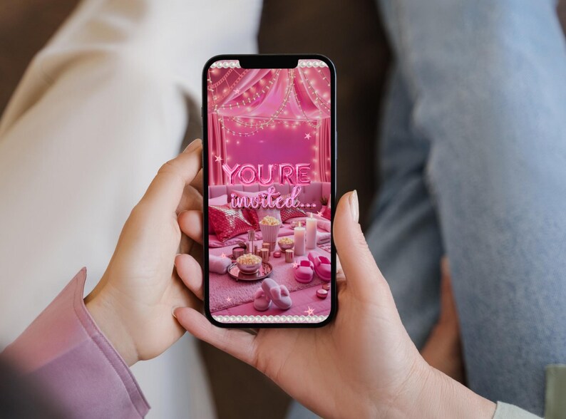 May include: A smartphone displays a pink invitation scene with the text "YOU'RE invited..." in a neon style. The scene includes a bed with pillows, candles, and popcorn. The phone is held by a person.