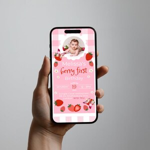May include: A smartphone displays a pink invitation for "Melissa's berry first Birthday." The design features a baby's photo, strawberries, and a checkered pattern. The invitation includes the date, time, and location details.