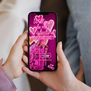 K&ouml;nnte beinhalten: Ein Smartphone zeigt eine Valentinstag-Grafik mit dem Text "Will you be my Valentine? Galentine?" in Neonrosa. Das Bild enth&auml;lt Herzen, einen Cocktail und ein Tic-Tac-Toe-Spiel, alles in einem leuchtenden Rosa.