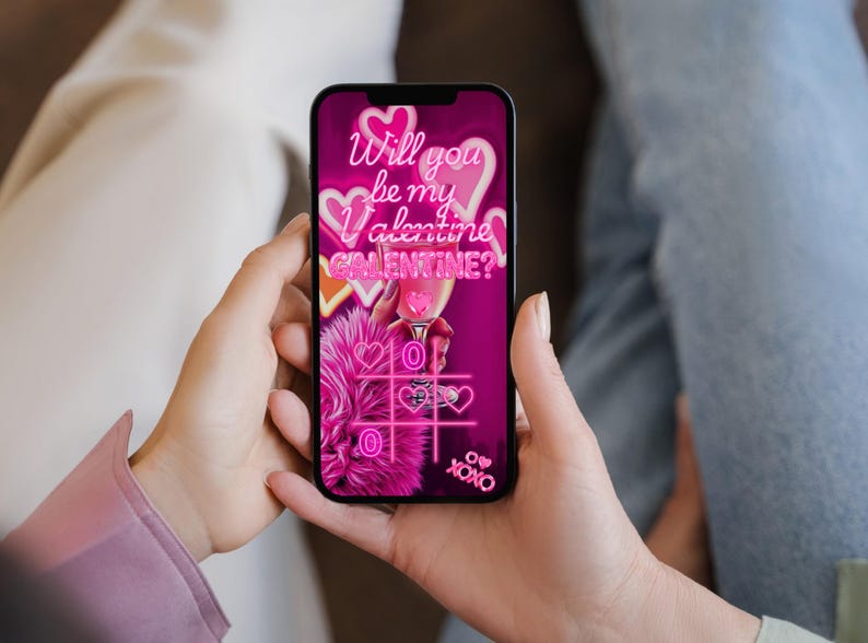 K&ouml;nnte beinhalten: Ein Smartphone zeigt eine Valentinstag-Grafik mit dem Text "Will you be my Valentine? Galentine?" in Neonrosa. Das Bild enth&auml;lt Herzen, einen Cocktail und ein Tic-Tac-Toe-Spiel, alles in einem leuchtenden Rosa.