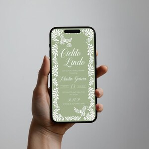 May include: A smartphone displays a digital invitation with the words "Cielito Lindo" in elegant script. The invitation features a sage green background with white floral and dove accents, perfect for a baby shower.