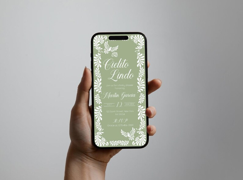 May include: A smartphone displays a digital invitation with the words "Cielito Lindo" in elegant script. The invitation features a sage green background with white floral and dove accents, perfect for a baby shower.