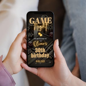 May include: A smartphone displaying a digital invitation for a game night party. The invitation features a black and gold design with playing cards, dice, and chips. The text reads "Game Night" and "You're invited to Oliver's 30th birthday 01/03/2025".