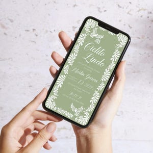 May include: A smartphone displays a digital invitation with the words "Cielito Lindo" in elegant script. The invitation features a sage green background with white floral and bird accents. The invitation includes the names Martin Garcia and the date.