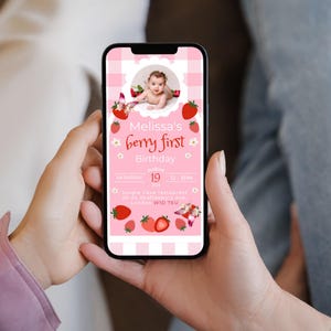 May include: A smartphone displays a pink invitation for "Melissa's berry first Birthday." The design features strawberries, flowers, and a baby's photo. The invitation includes the date, time, and location details, all set against a gingham background.