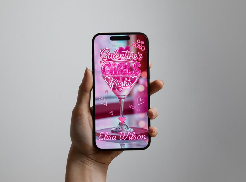 Op de afbeelding: Een smartphone toont een roze afbeelding voor een Galentine's Girls Night. Het ontwerp bevat een martini glas gevuld met roze glitter en de tekst "Galentine's Girls Night" in een sierlijk lettertype. De naam "Elisa Wilson" wordt ook weergegeven.