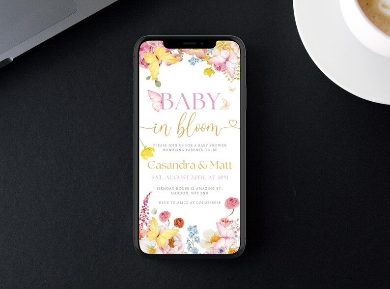 K&ouml;nnte beinhalten: Ein Smartphone zeigt eine Babyparty-Einladung. Der Text "BABY in bloom" ist in Rosa und Gold gehalten und von Aquarellblumen und Schmetterlingen umgeben. Die Einladung enth&auml;lt die Namen der Eltern, Datum, Uhrzeit und Ort.