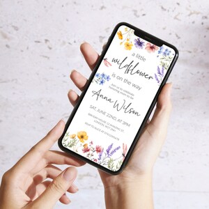 Puede incluir: Una invitaci&oacute;n digital con un dise&ntilde;o floral que presenta una ilustraci&oacute;n de acuarela de flores silvestres en tonos azules, amarillos, rosas y morados. El texto dice "a little wildflower is on the way" e incluye el nombre "Anna Wilson" y los detalles de un baby shower el 22 de junio a las 3 pm.