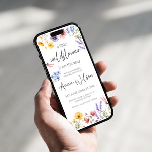 Puede incluir: Una invitaci&oacute;n de baby shower blanca con un borde floral. El texto dice "a little wildflower is on the way" e incluye el nombre "Anna Wilson". La invitaci&oacute;n detalla la fecha, la hora y la ubicaci&oacute;n del evento.