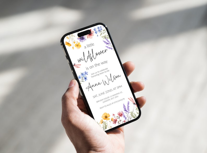 Puede incluir: Una invitaci&oacute;n de baby shower blanca con un borde floral. El texto dice "a little wildflower is on the way" e incluye el nombre "Anna Wilson". La invitaci&oacute;n detalla la fecha, la hora y la ubicaci&oacute;n del evento.
