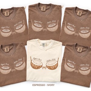 May include: A collection of brown and ivory t-shirts with a coconut bra design. Each shirt features the text "Megan's Bach Malibu 2026". A delicate necklace is draped on each shirt. The bottom of the image reads "ESPRESSO - IVORY".