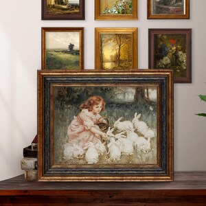 May include: A framed painting of a young girl in a pink dress feeding a group of white rabbits in a forest setting.