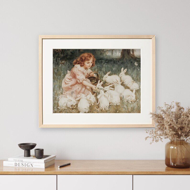 May include: A framed painting of a young girl in a pink dress feeding a group of white rabbits in a grassy field.
