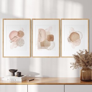 May include: Three framed abstract watercolour prints with a neutral colour palette of brown and pink. The prints feature geometric shapes and abstract patterns.