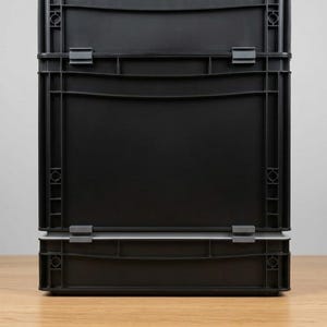 Könnte beinhalten: Ein Stapel aus zwei rechteckigen schwarzen Kunststoff-Aufbewahrungsboxen mit verstärkten vertikalen Rippen und kleinen grauen Verschlussclips an den Seiten. Die Boxen verfügen über eine solide Frontplatte mit glatter Oberfläche und Rahmen.