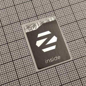 Pode incluir: Um autocolante retangular preto com um design geométrico branco e a palavra "inside" em texto branco. O autocolante está sobre um fundo de grelha cinzenta.