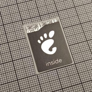 Op de afbeelding: Een rechthoekige sticker met een donkergrijze achtergrond en een wit voetlogo. Het woord "inside" is in het wit onder het logo gedrukt. De sticker bevindt zich op een grijze rasterachtergrond.