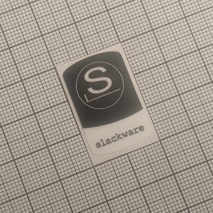 Peut inclure: Autocollant rectangulaire avec un fond noir et un "S" blanc à l'intérieur d'un cercle. En dessous du cercle se trouve une coche. Le mot "slackware" est imprimé en blanc en bas de l'autocollant.