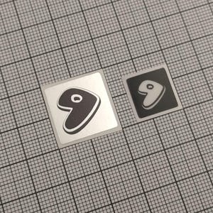 May include: Two square stickers with a stylized number nine design. One sticker has a silver background with a black number nine outlined in white. The other sticker has a black background with a white number nine outlined in black.